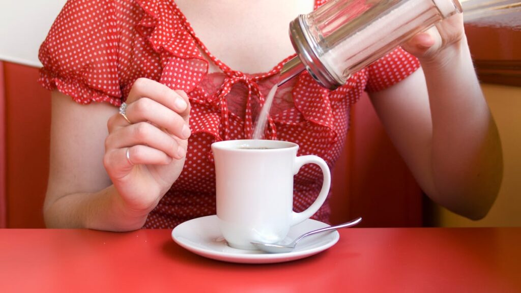 A person pours sugar into their coffee at a diner