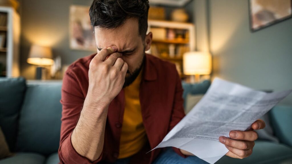 Stressed man rubs his forehead after opening and reading a letter.