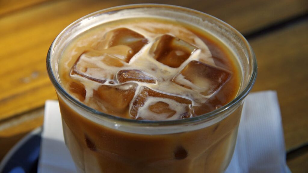 A close-up of ice cubes in a glass of coffee on a napkin on a wood table.