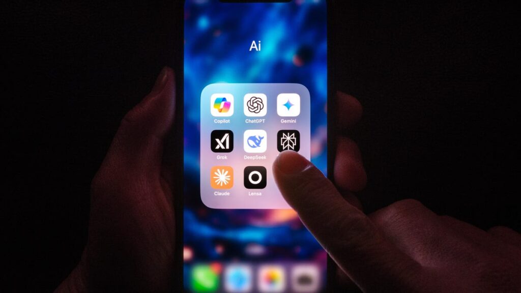 two hands hold a smartphone in a dark area. the screen is lit up and says AI above a window full of different LLM chatbots like OpenAI and Claude