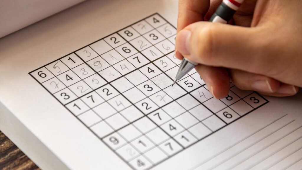 A person solves a paper sudoku puzzle by hand.