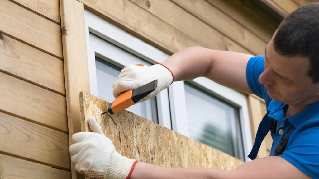 A man screw protective plywood onto a home window.