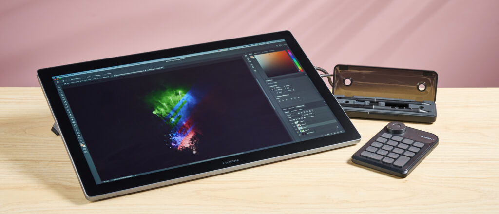 The Huion Kamvas Pro 19 featuring artwork of recolored fireworks, next to the the stylus case and Huion Keydial Mini shortcut remote, in front of a pink background.