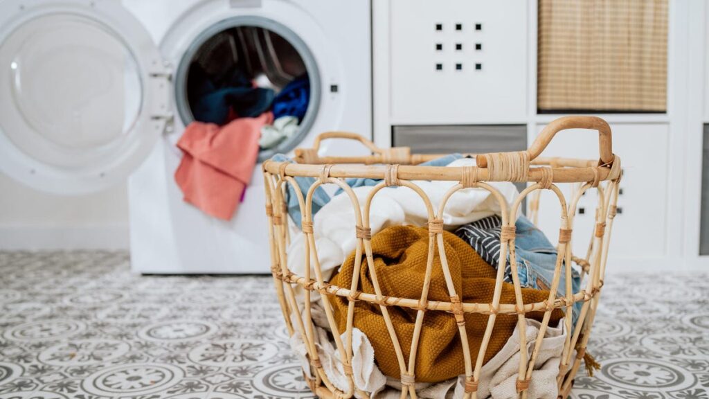 Close-up of colorful clothes in basket, open washing machine standing in background