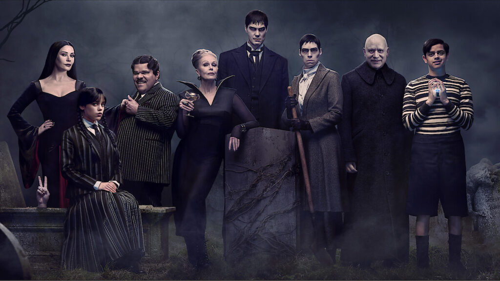 The cast of Wednesday posing in front of a gothic backdrop