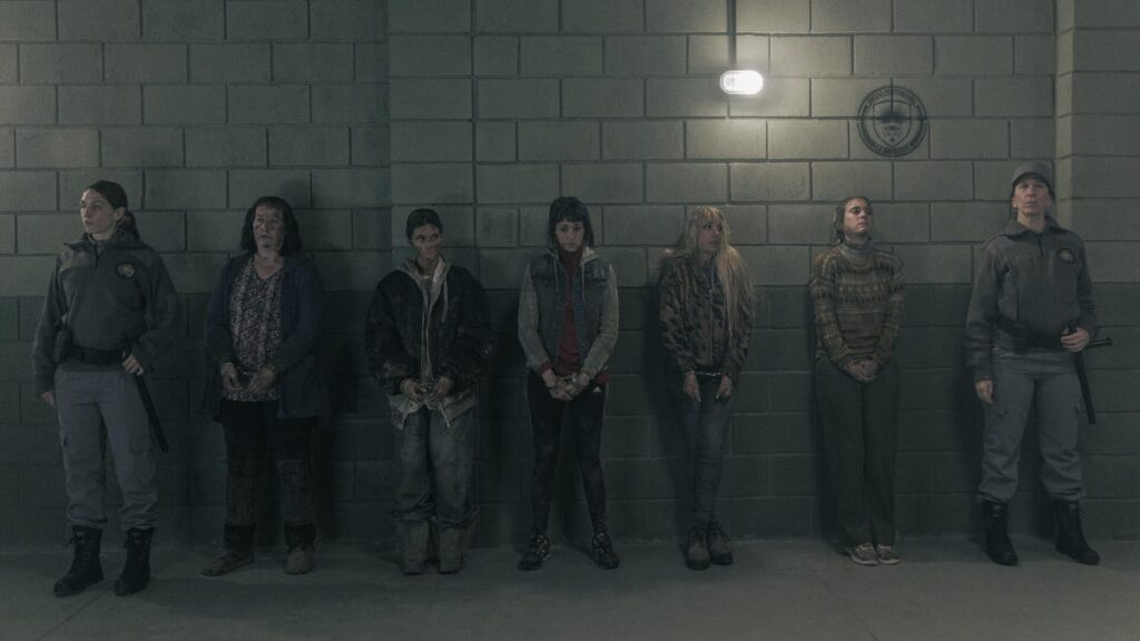 A group of female prisoners stand handcuffed in front of a wall