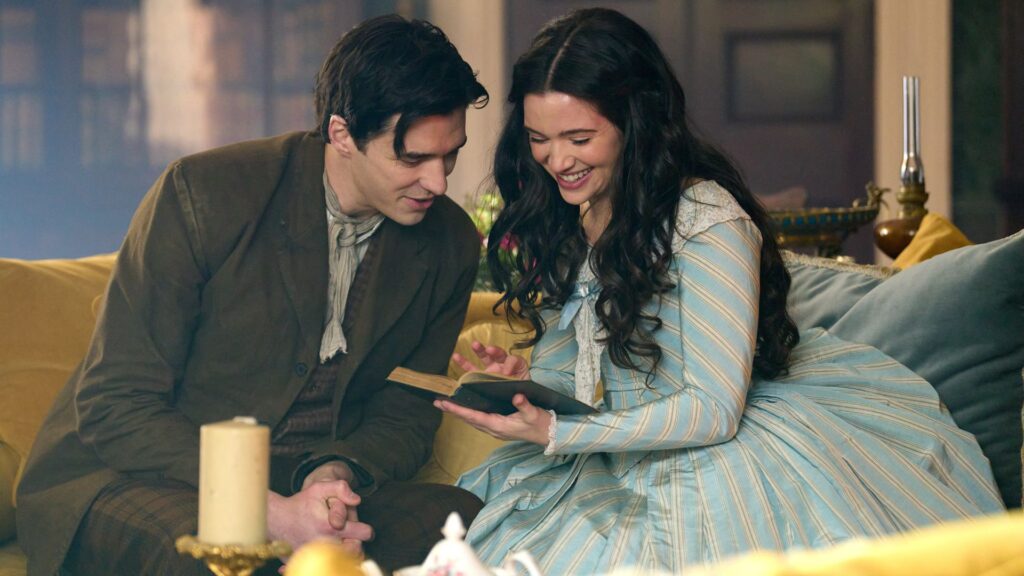 Cora and Liam laugh while reading a book on a sofa