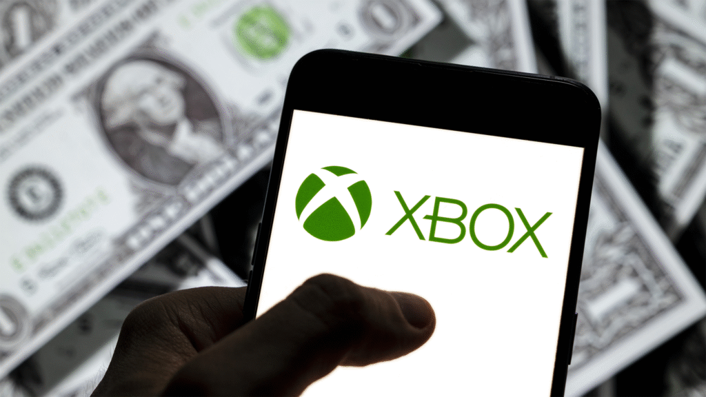 An Xbox logo on a phone, with dollar bills in the background