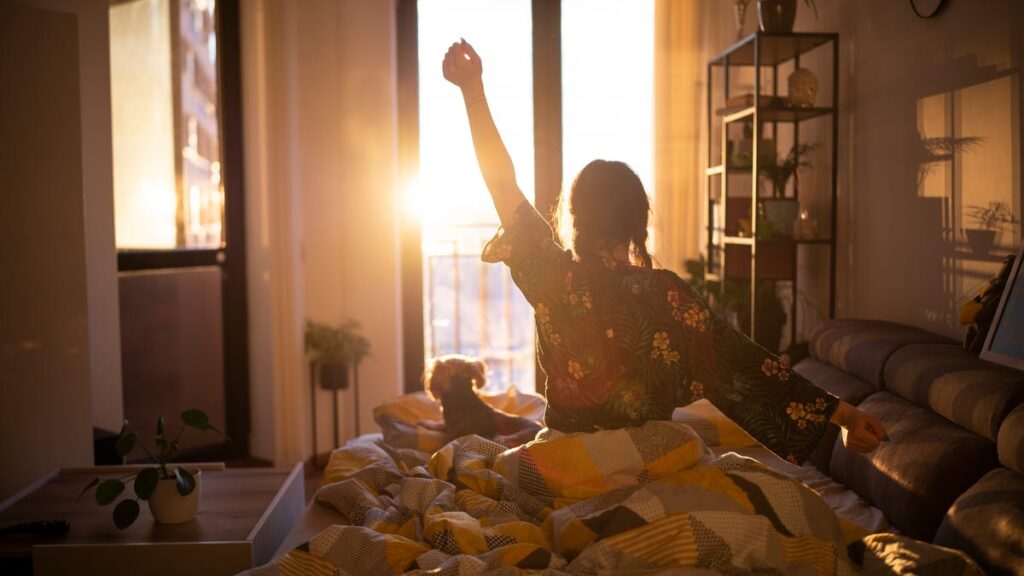 Woman stretching in bed after waking up to the morning sun