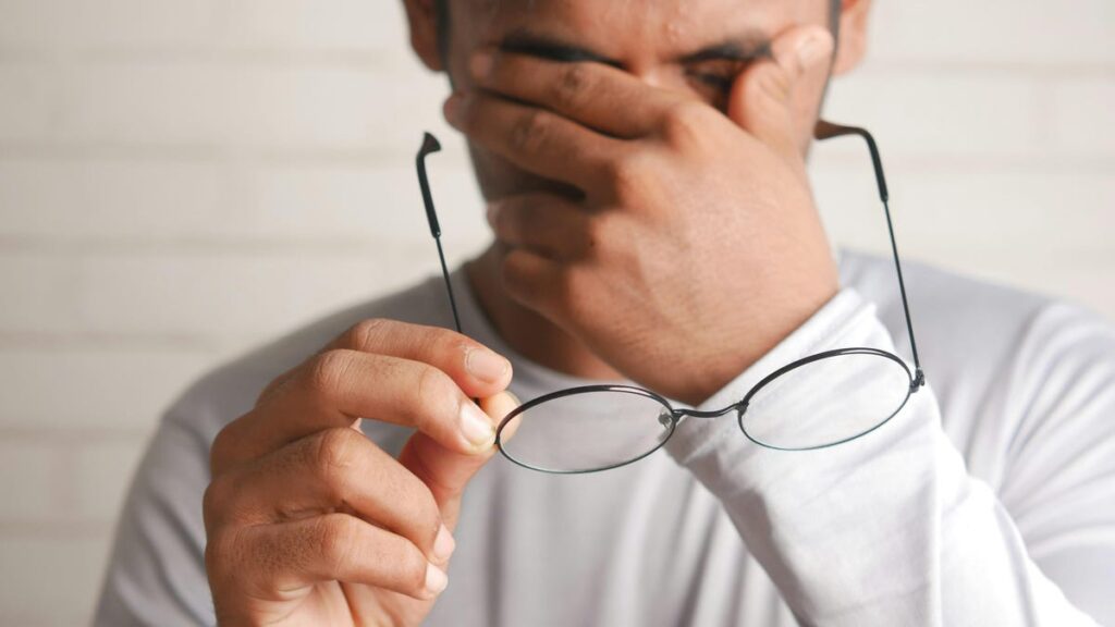 A person rubbing their eyes and holding their glasses.