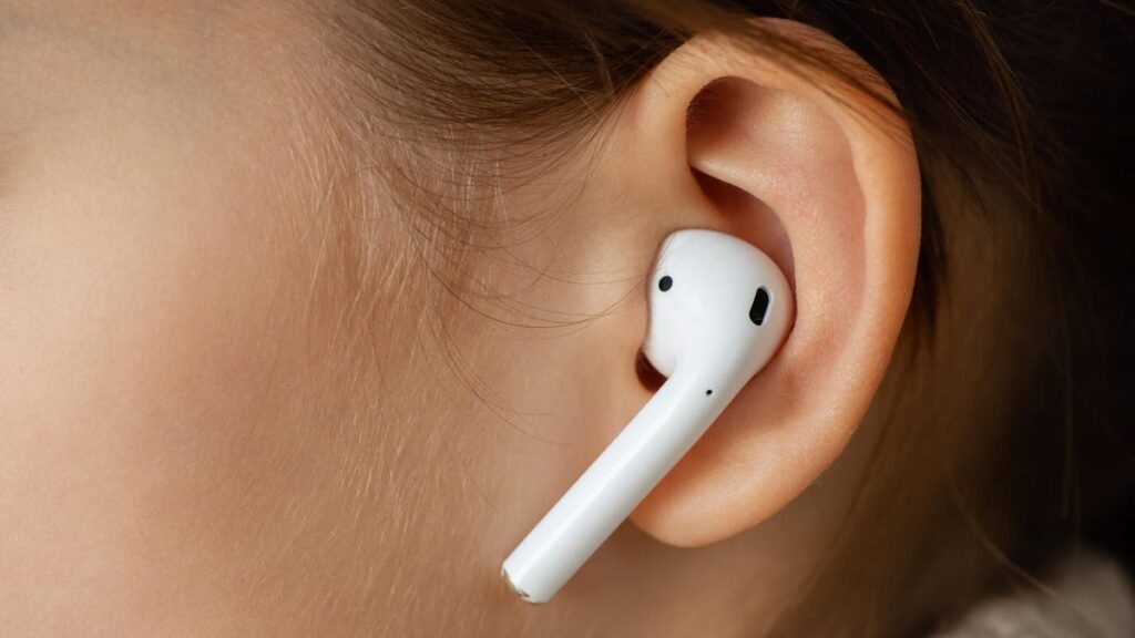 A white AirPod in an ear surrounded by brown hair.