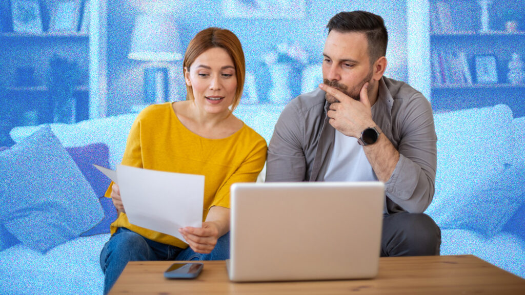 Couple looking at bills whilst sitting on a sofa, in front of a laptop