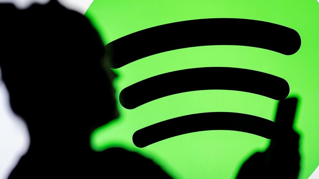 the silhouette of a person looking at their phone sits atop of the green Spotify logo