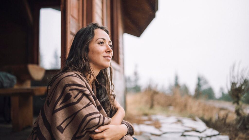 A woman sits on a porch outside a home on a cloudy, wet day.