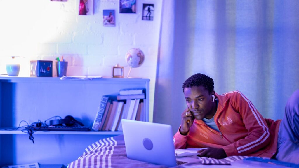 How to Use AI to Manage Your Time as a Student An image of a man studying on his bed, purple lighting gettyimages-1356515335