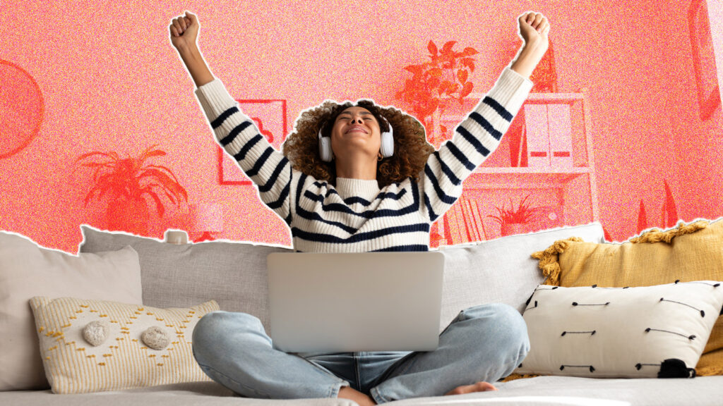 A young woman sitting on a sofa, wearing headphones and throwing her arms excitedly into the air.