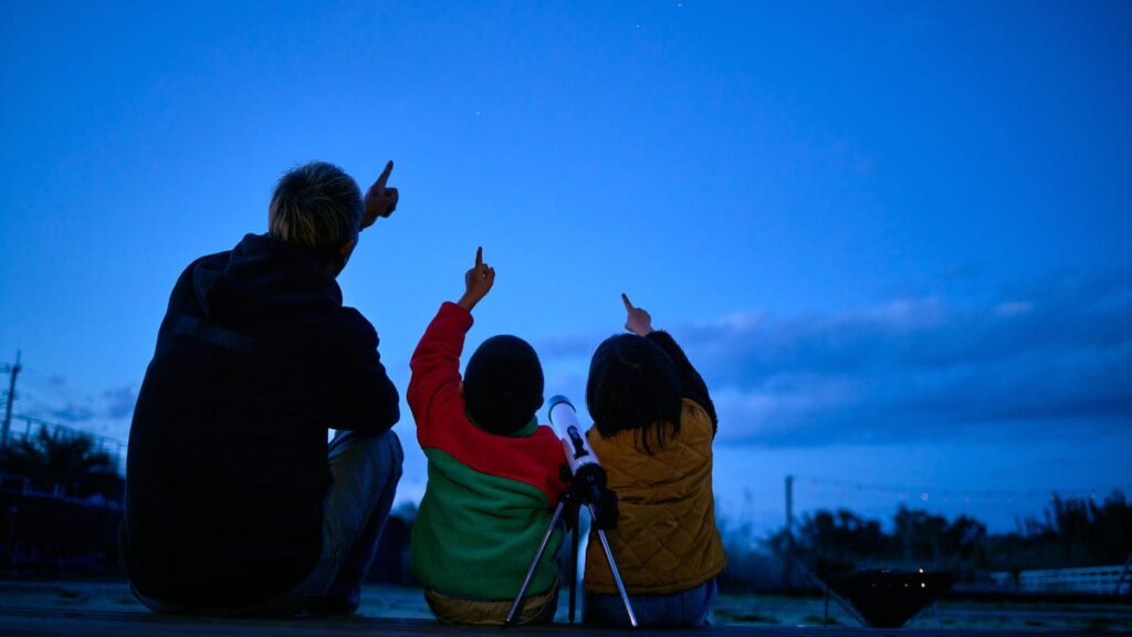 Family is seen sitting outside looking up at the sky