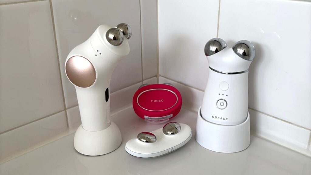 A person with an orange-red bob haircut using a white microcurrent device on their jawline.