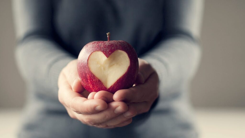 5 Heart Healthy Foods to Naturally Boost Your Heart Health Hands holding an apple with a heart-shaped cutout.