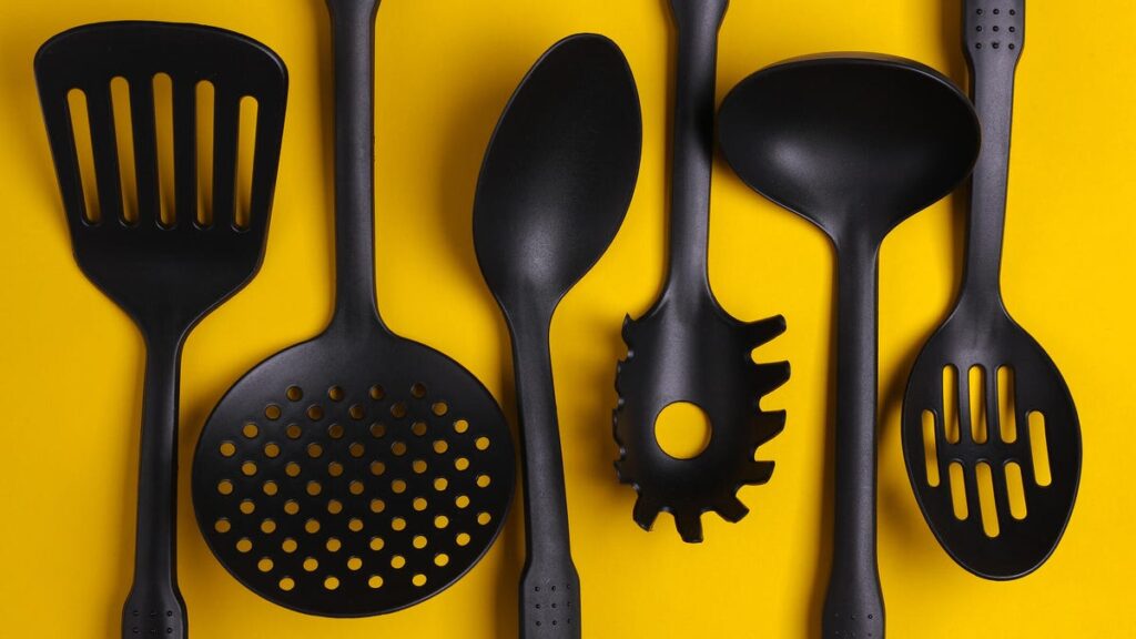 Avoid Microplastics, Bacteria and More: 8 Kitchen Tools You Need to Replace ASAP Black plastic kitchen tools on yellow background. Top view. Flat lay