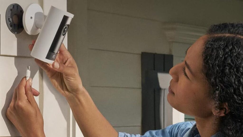 A woman plugs in an outdoor Ring camera connected to exterior siding.