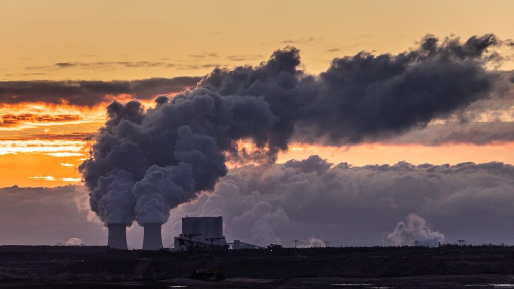 The sky is orange with sunset streaks, and in the foreground there's an industrial plant pumping thick clouds of smoke into the air. They're smoke clouds nearly indiscernible from natural clouds.