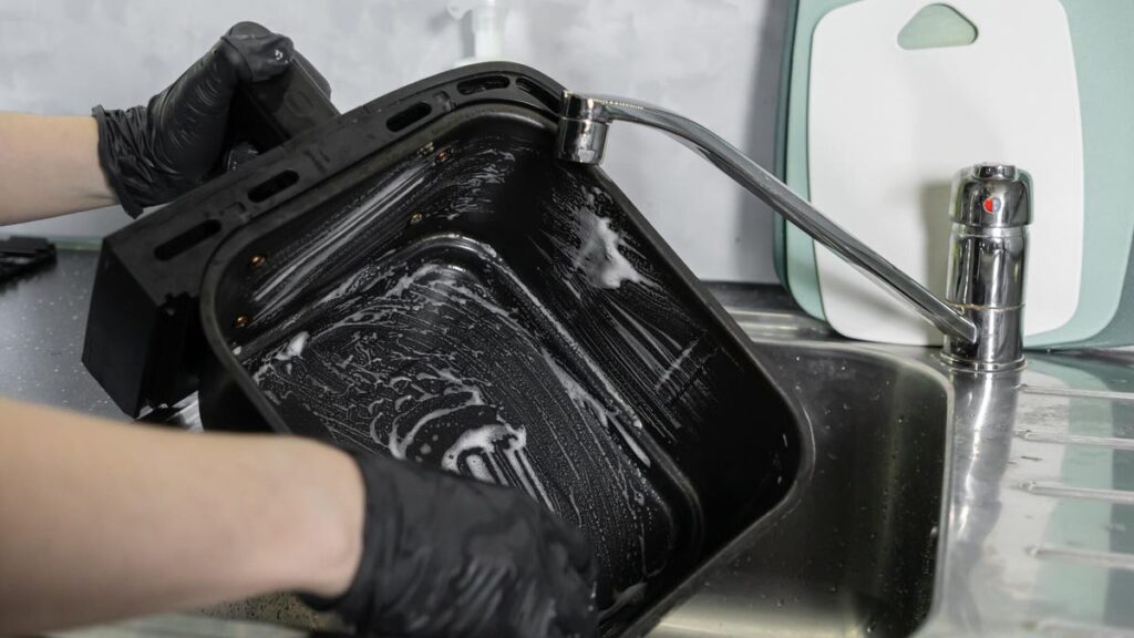person cleaning air fryer basket in sink