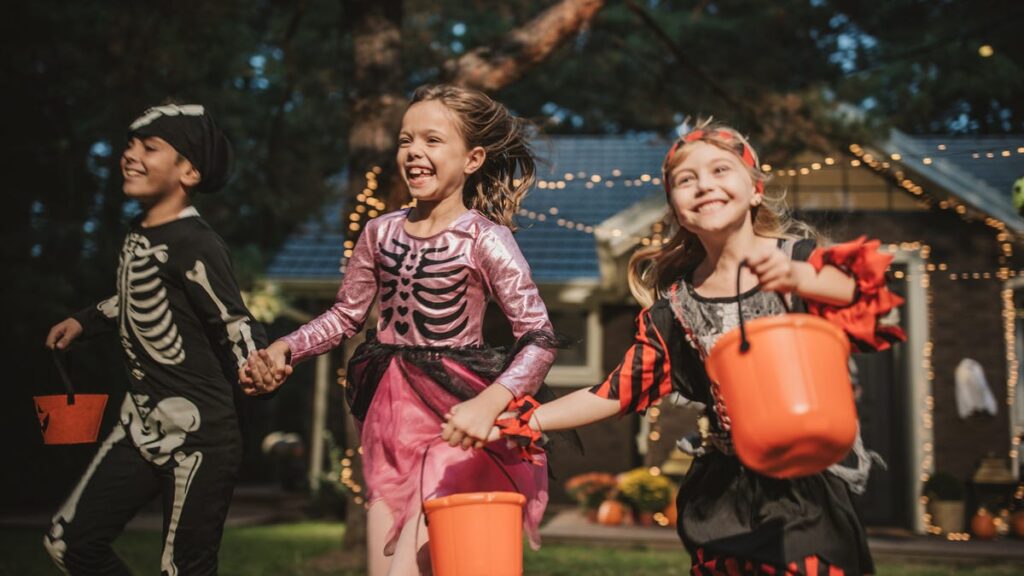 Three trick or treaters in costume running through a neighborhood.