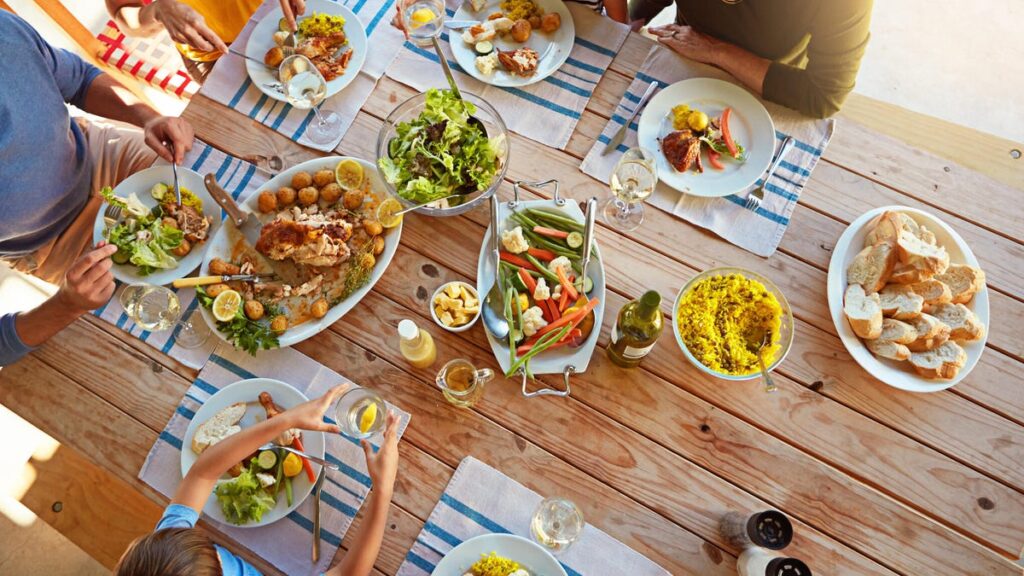 A photo of a dinner table filled with meals, with a family sitting around it (gettyimages-685577152)