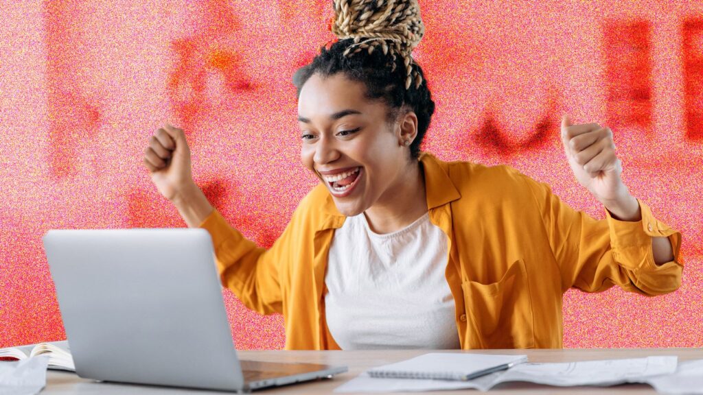 Young woman sitting at a computer desk looking excited in front of laptop.