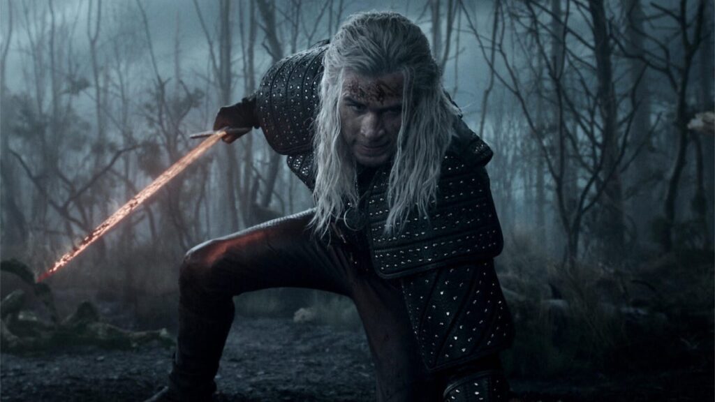 A promotional still from The Witcher Season 4 showing Liam Hemsworth scrounging down, holding a sword.