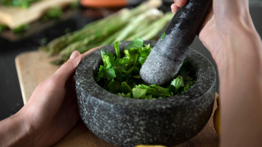person crushing herbs with pestle and mortar