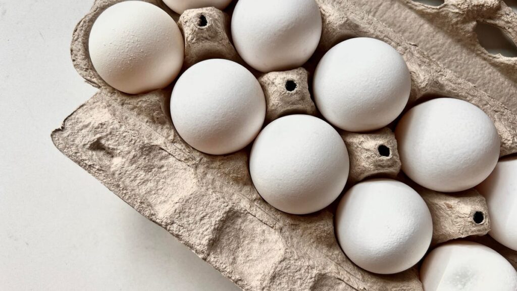 A carton of 12 fresh eggs sit on a table.