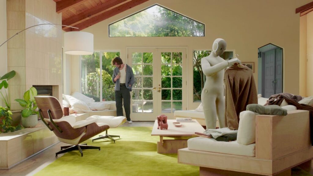 A humanoid robot folds laundry in an upscale living room.